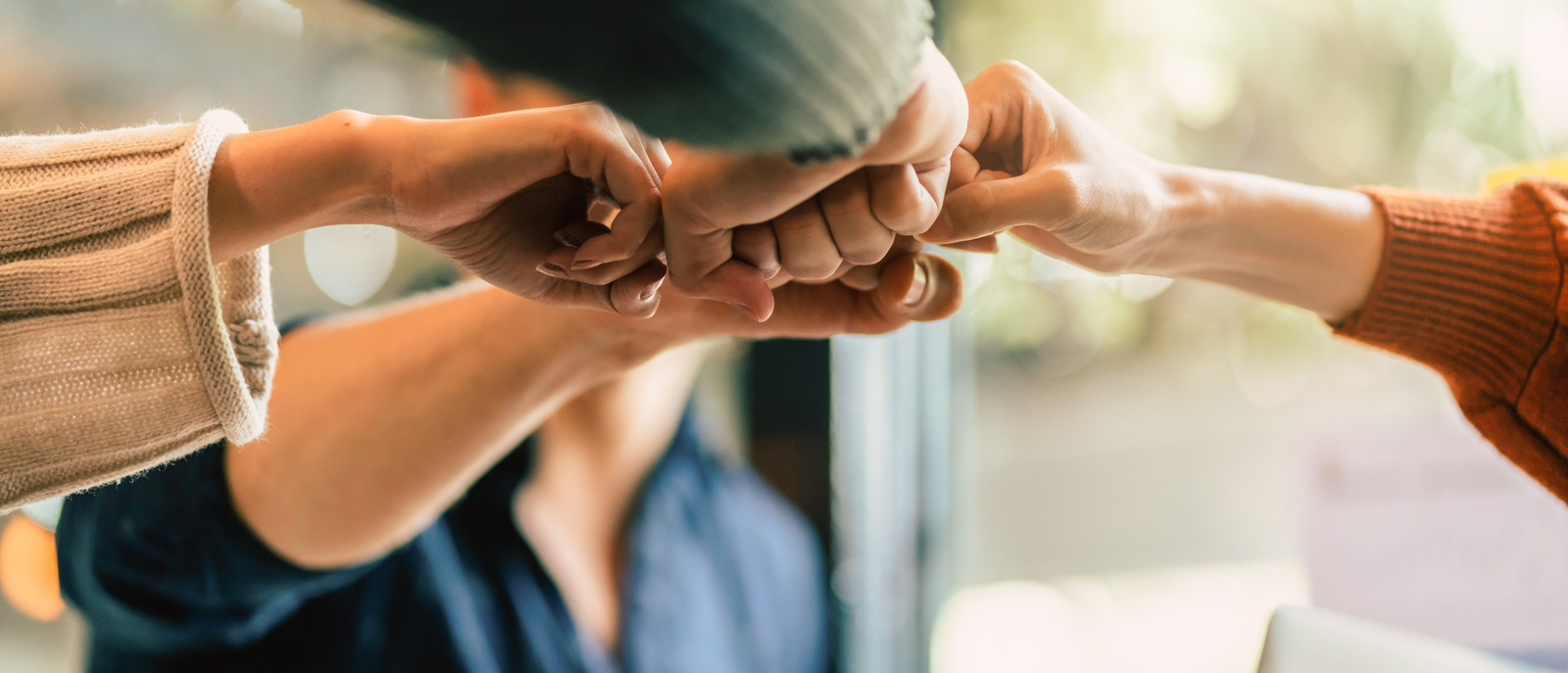 Vier Personen strecken sich gegenseitig die geballten Fäuste entgegen und treffen sich in der Mitte zu einem gemeinsamen Fistbump.