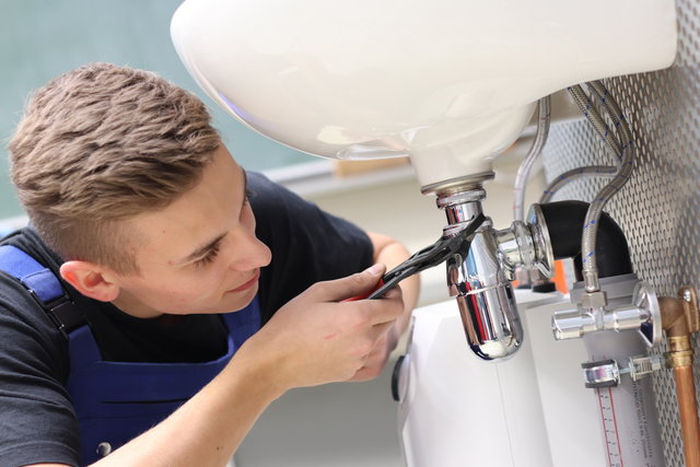 Ein Teilnehmer kniet vor einem Waschbecken und repariert den Abfluss mit Werkzeug.