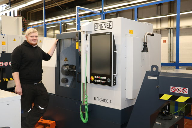 Ein Teilnehmer steht im Metallbereich vor der CNC-Drehmaschine Spinner TC400 und lächelt in die Kamera.