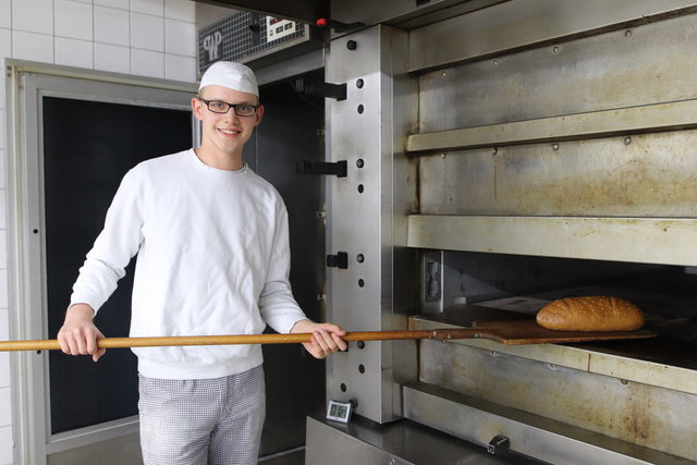 Ein Teilnehmer holt mit einem Brotschieber ein frisch gebackenes Brot aus dem Backofen in der Backstube.